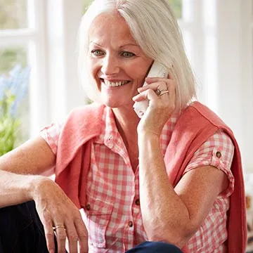 a seated older woman smiling and talking on the phone