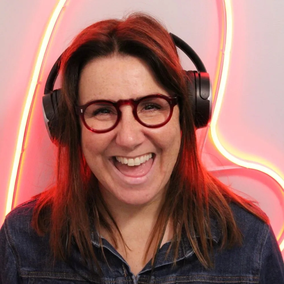 Wearing headphones, Katie Phillips smiles beside a wall with neon lights