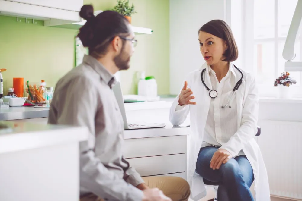 A doctor in a white lab coat speaks with a man in a doctor's office