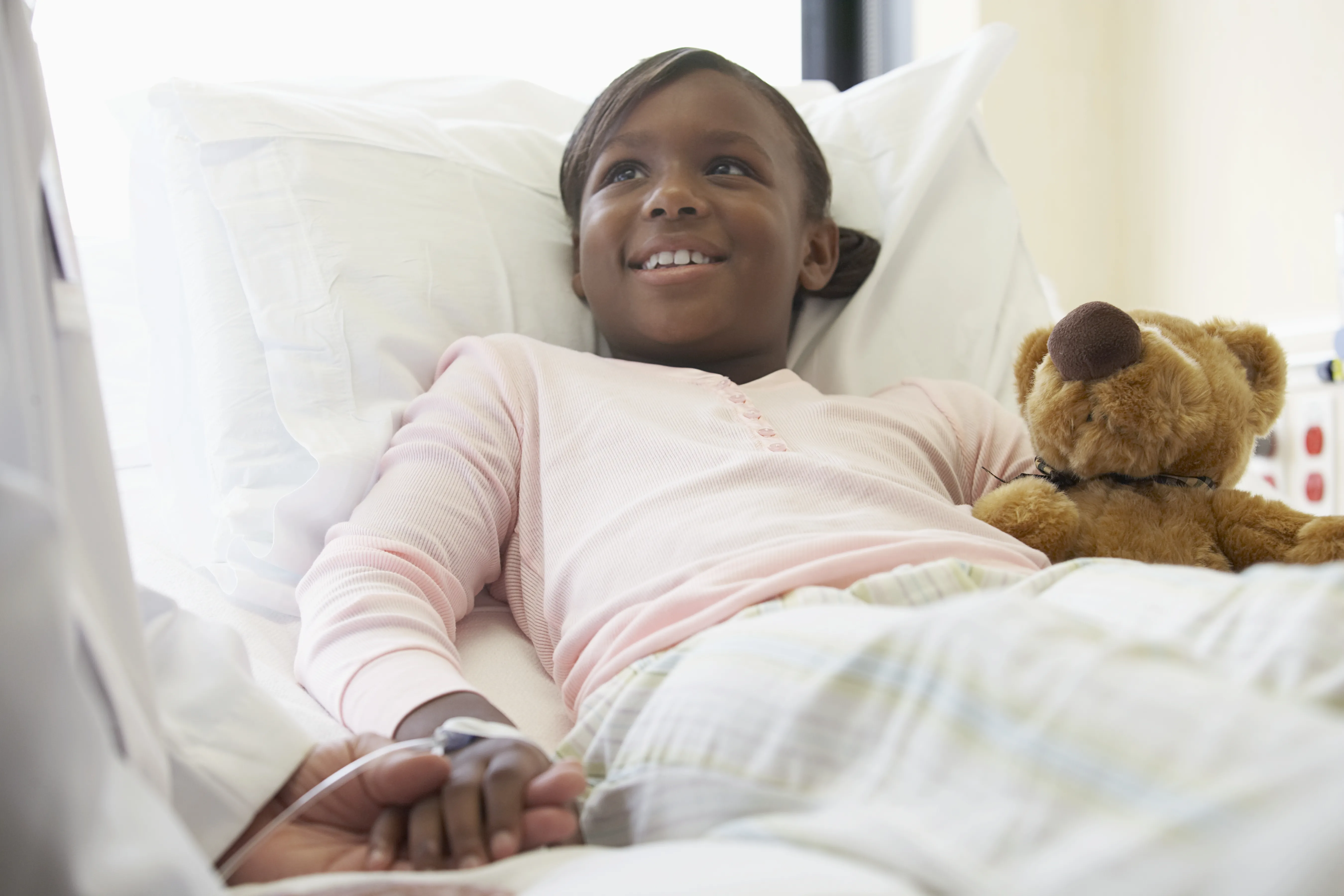 a smiling girl in a hospital bed with a teddy bear