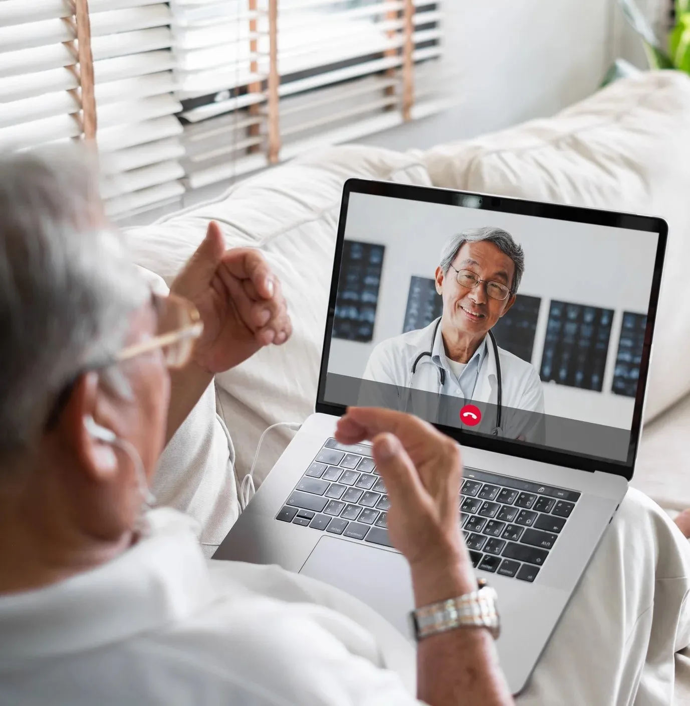 An older adult male wearing glasses talks with a doctor during a video call on a laptop