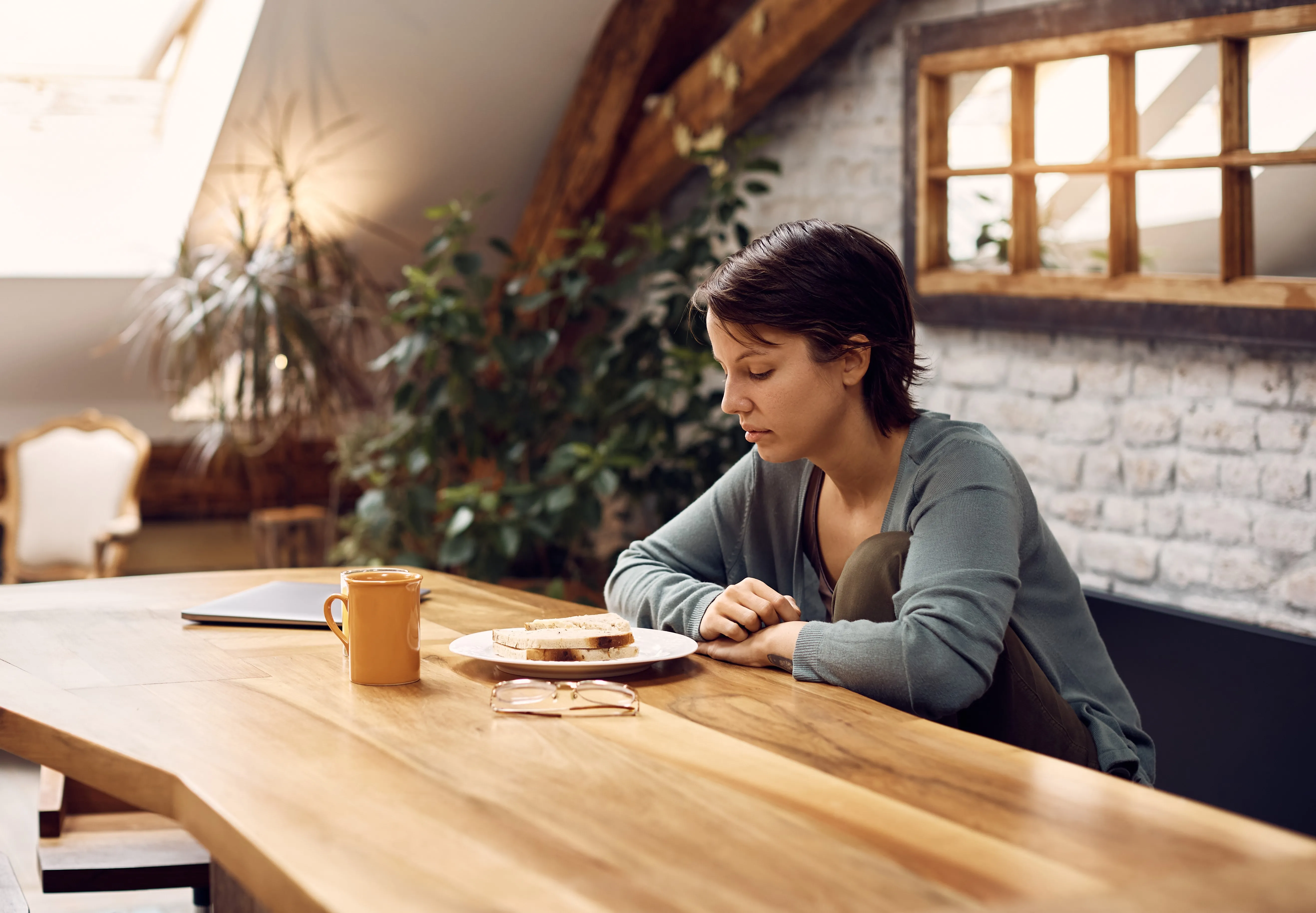 A woman stares without interest at a plate of food on a kitchen table