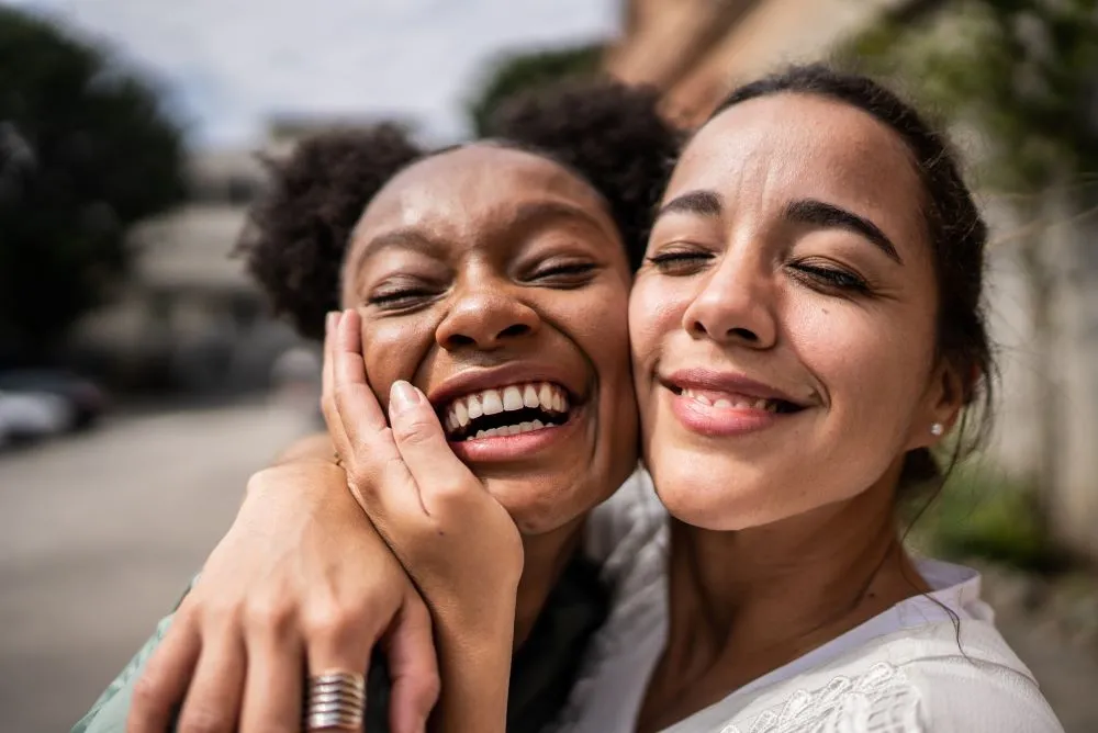 Two young smiling friends hug cheek to cheek