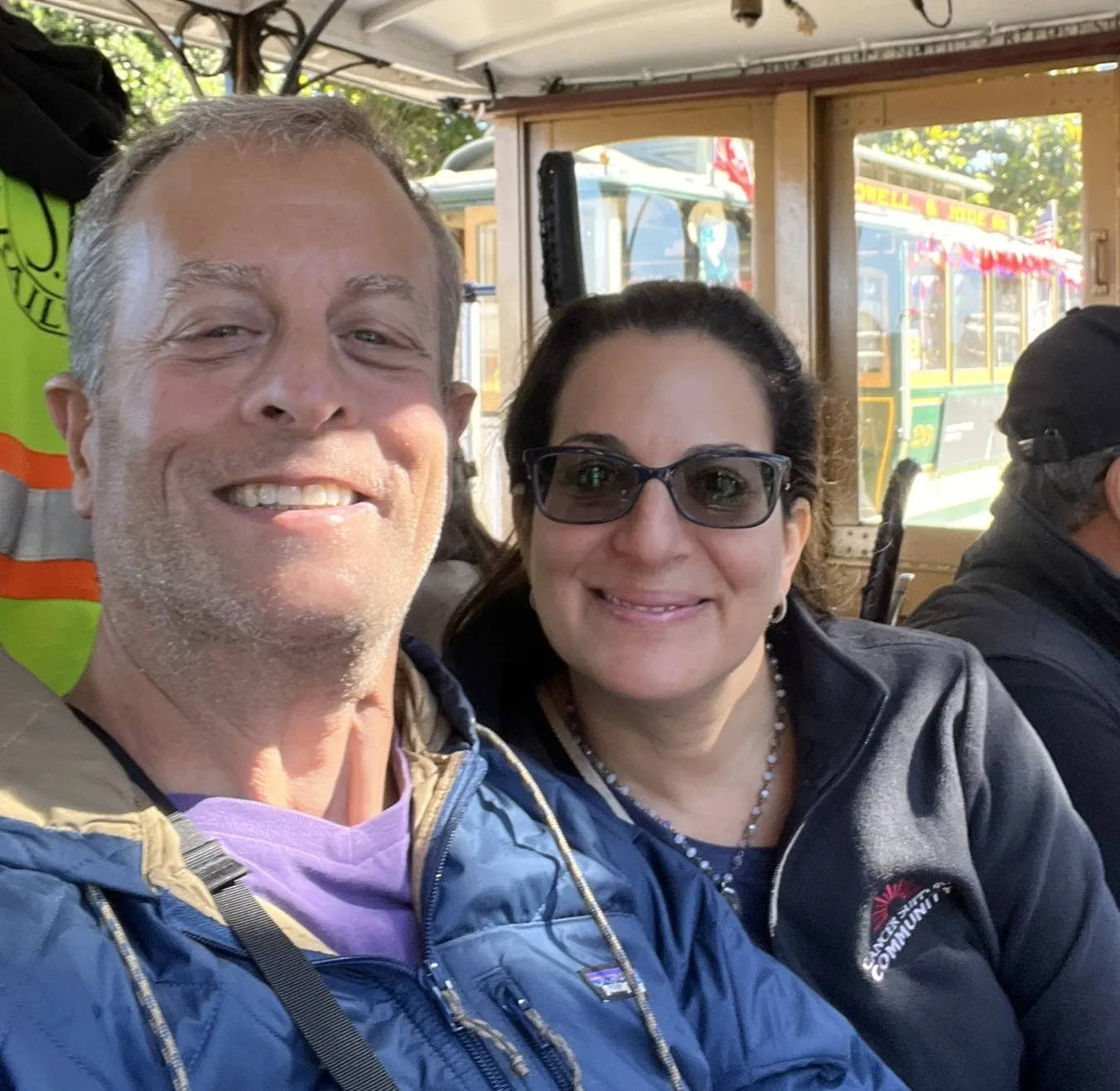 Heather and Rich smile from their seats on a San Francisco cable car