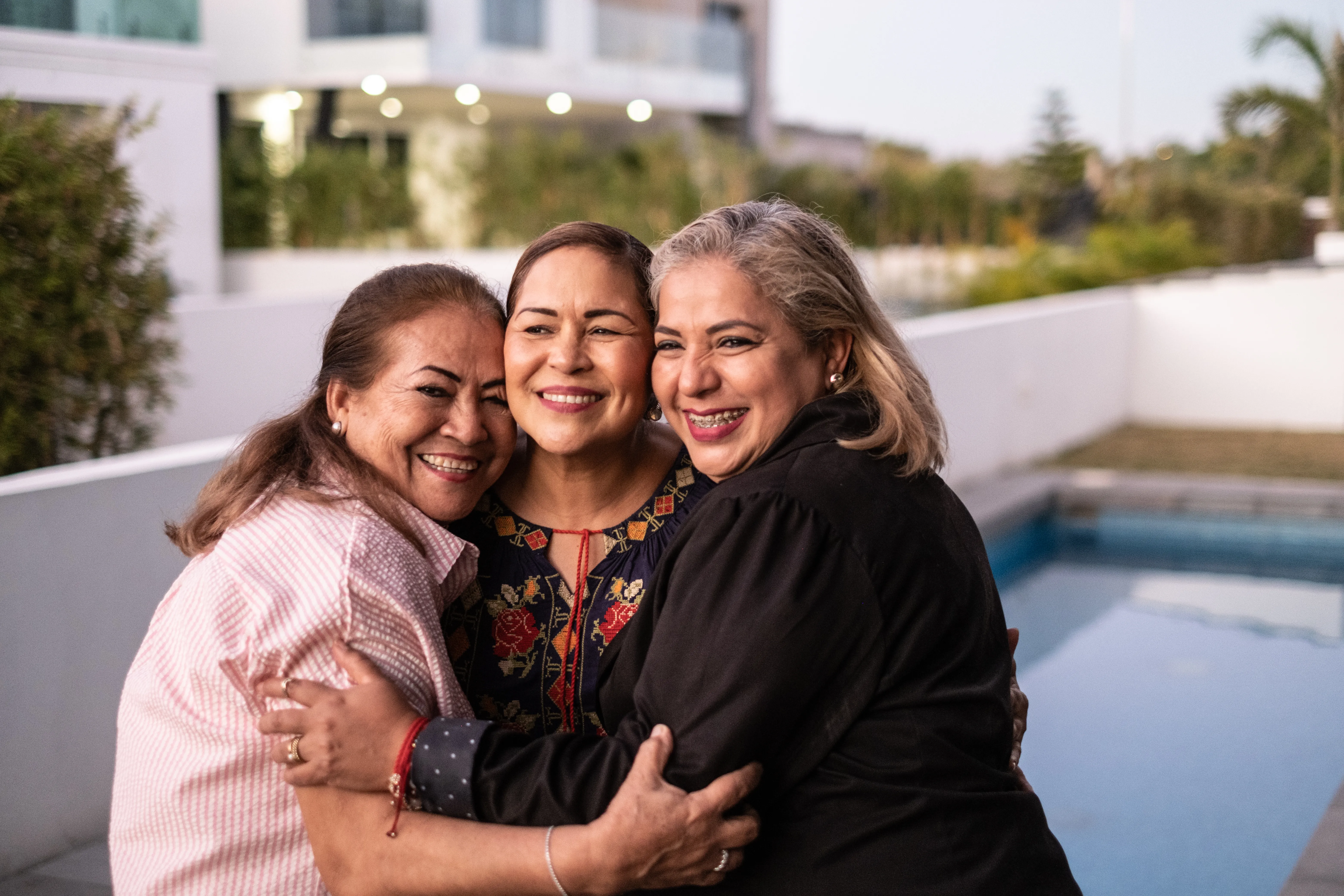 Three smiling women friends stand arm in arm on an outdoor deck