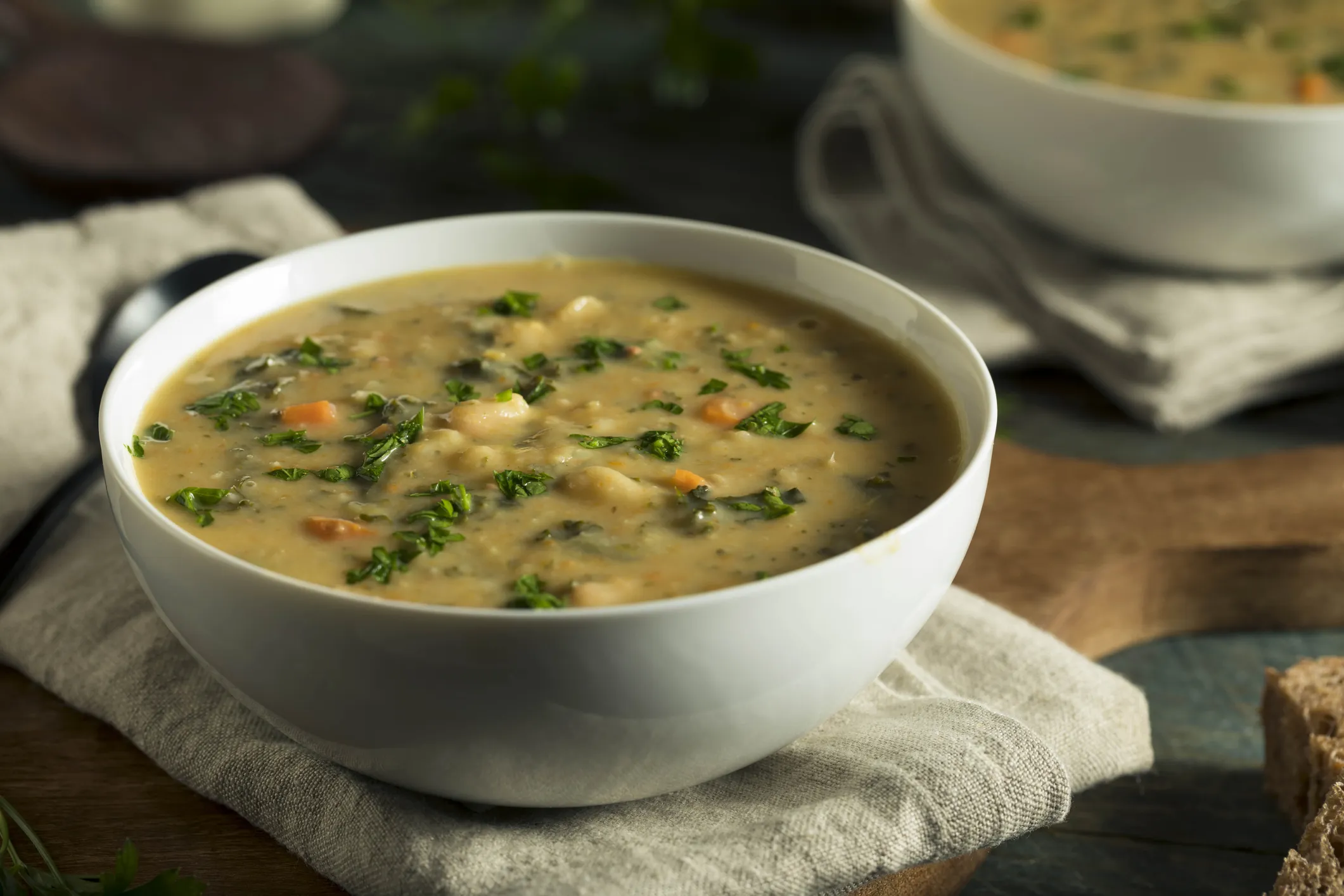 A ceramic bowl filled with a soup containing greens and white beans