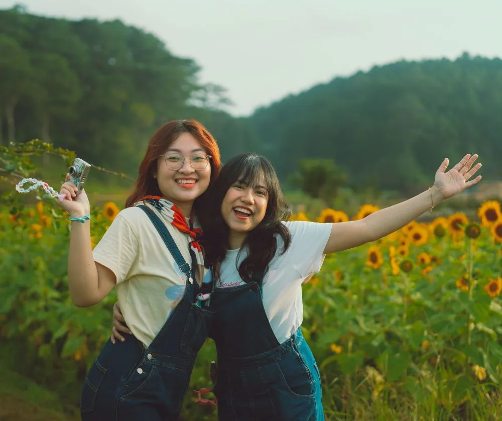 Two friends smile for a photo in a field of sunflowers
