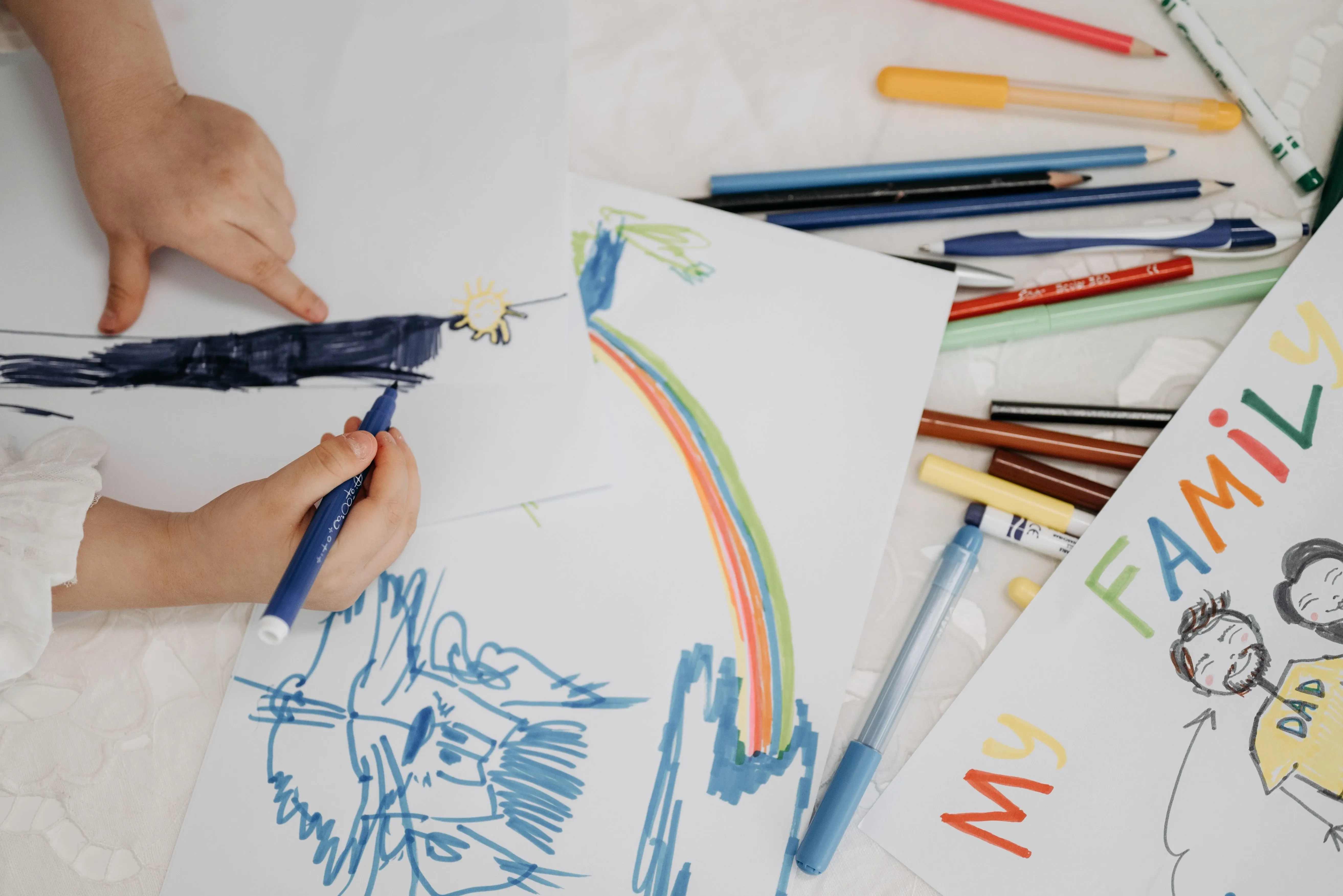 Child's small hands hold a marker while creating a colorful drawing