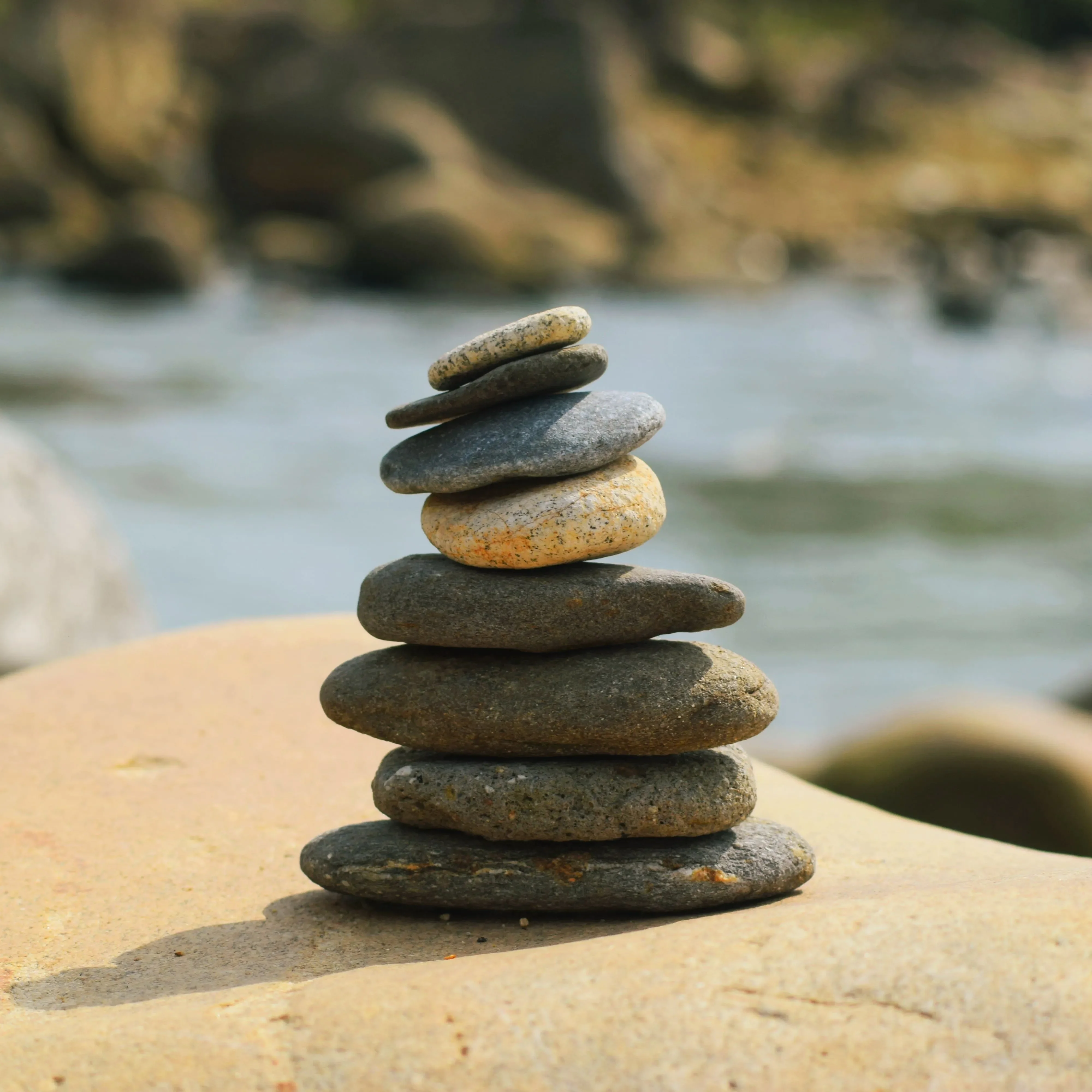 A stacked pile of stones sits on a large rock beside a river