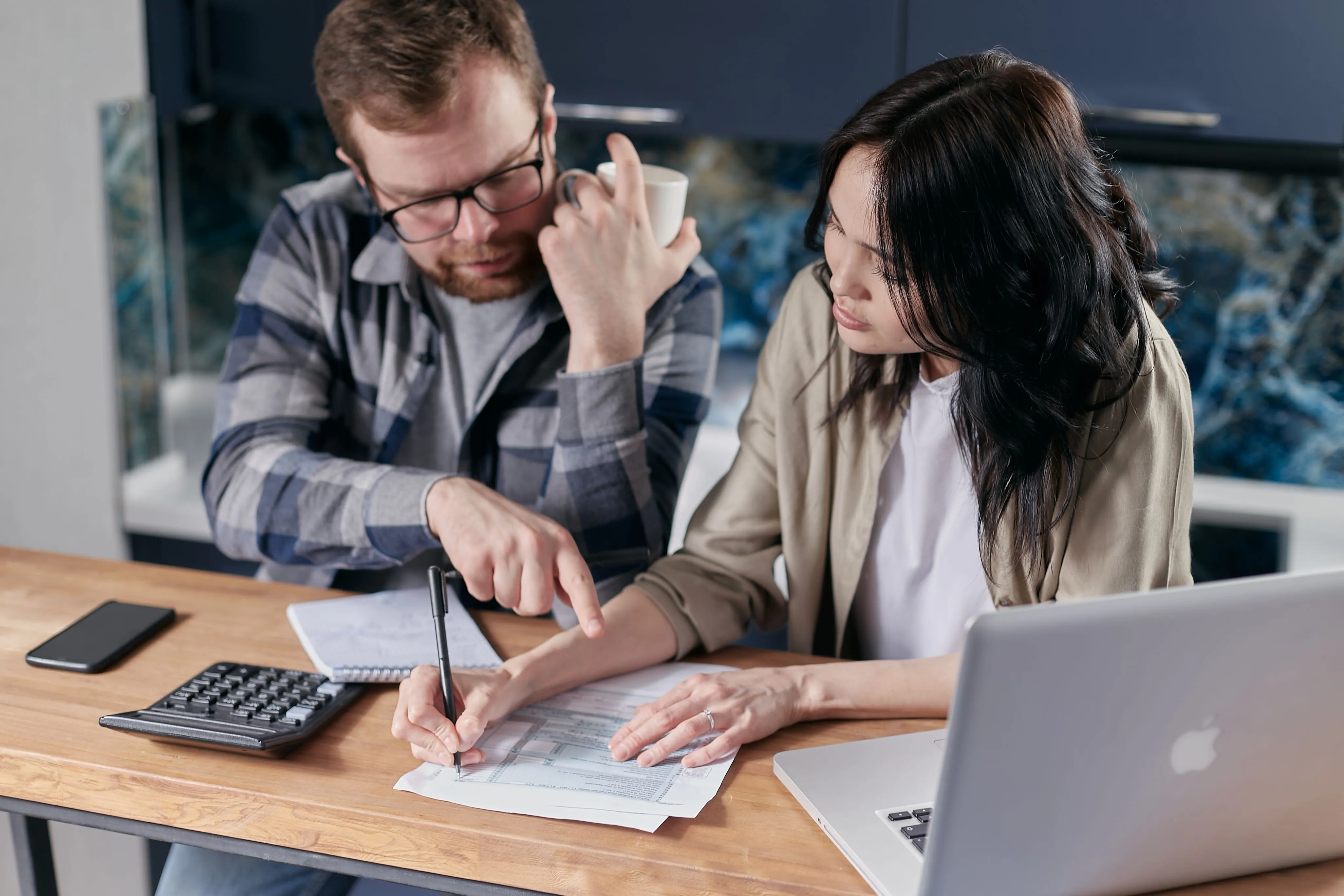 A man and a woman seated at a counter with a calculator discuss paperwork