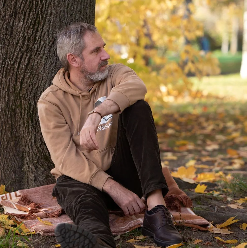A man quietly reflects beneath a tree in autumn