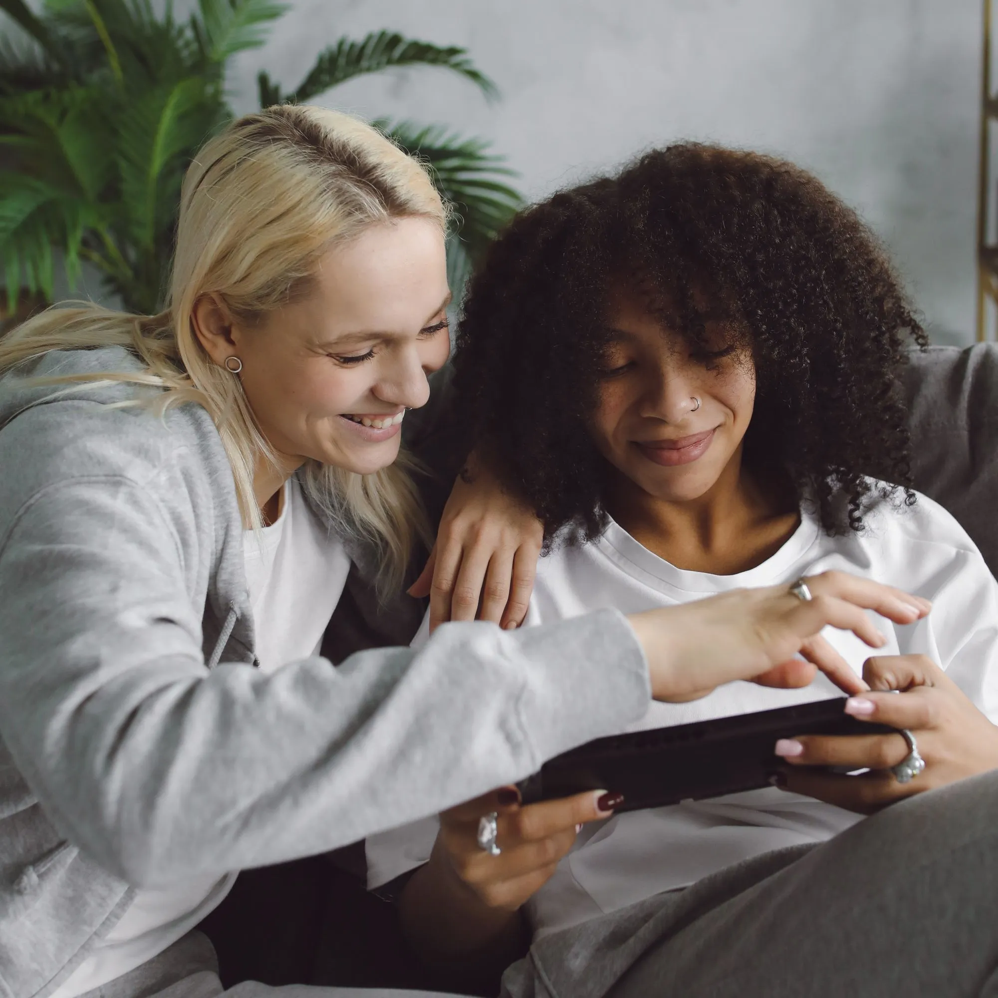 Two friends sit beside one another looking at a digital tablet