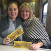 young white woman and older white woman embracing, smiling and holding yellow tickets 