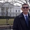 white man wearing a coat and tie in front of white house 