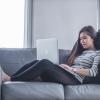 asian woman on a grey couch working on her laptop