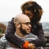 An African American couple snuggles in front of a tree-lined backdrop