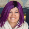 Amber smiles from inside her home with bright purple hair.