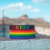 Pride Month wristbands rest on a stone wall beneath a blue sky