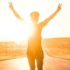 A women's silhouette shines against a sunny horizon as she raises her arms triumphantly in the air