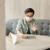 A young man wearing a mask speaks to someone on his mobile phone while sitting at home