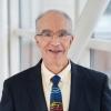 Dr. Stephen Edge wears a suit and tie and smiles beside a window within a modern building