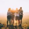 Group of 4 people stand with their arms around each other and their backs turned, facing the sunlight.