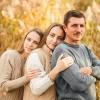 A father and his daughters stand beside one another in front of a sunlit field of grass