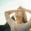 Woman with glasses on raises arms behind her head, closes her eyes, and breathes.