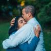 A man hugs his wife outdoors in a tree-lined yard
