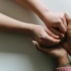 A woman's hands comfortingly hold the hands of a friend