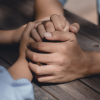 Hands fold over another pair of hands in a comforting manner