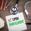 An open enrollment sign rests on a desk beside a stethoscope and several colored pencils