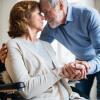 Senior couple at home with husband caring for wife in wheelchair