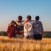 Friends stand side by side with their arms around one another, looking out at a blue sky