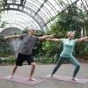 A senior couple stretch out on their yoga mats in an indoor arboretum
