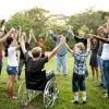 A group of people reflecting diverse ages and races stands in a circle, clasps one another's hands in unity and raises them to the sky