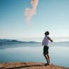 A man in white shirt and shorts stretches out his arms and looks up at the blue sky smiling beside a lake