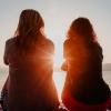 Two women friends sit together looking out at a lake as the sun sets