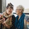 Two women friends laugh together beside a window while looking at their smartphone