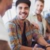 Four young men sit together beside a window laughing and talking together