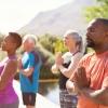 A group of men and women of different ages practices yoga and meditation outside in the sunshine