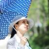 A young woman wears a white hat and carries a blue umbrella to shield her face from the sun