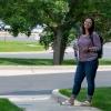 Amber smiles while standing on a sidewalk in front of a leafy green tree in the summer sunshine 