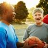 Three men in athletic clothing stand together on a sunlit basketball court.