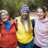 A diverse group of women smiling in jackets outdoors with their arms around one another