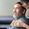 A woman gently rests her hand on a man's shoulder in a comforting way