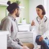 A doctor in a white lab coat speaks with a man in a doctor's office
