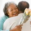 A woman smiles and hugs a man as she holds a bouquet of roses