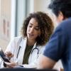 A female doctor in a white coat shows a male patient information on a tablet screen