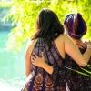 A woman wearing a colorful head scarf embraces her sister along the bank of a sunlit river